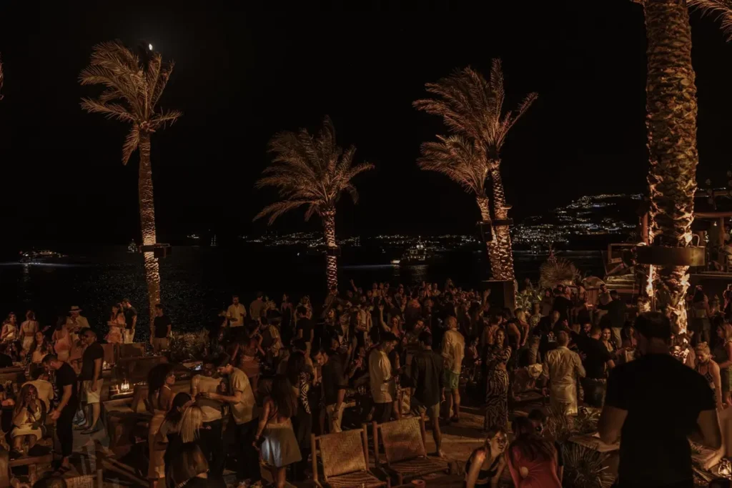 Guests gathered beneath illuminated palms on Scorpios's outdoor terrace after dark