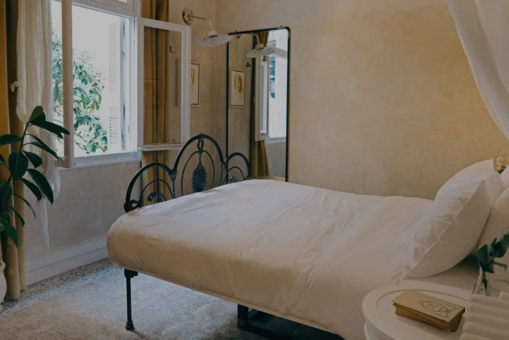 An antique metal bed, soft curtains and potted plants in Shila’s Attic Antique suite.