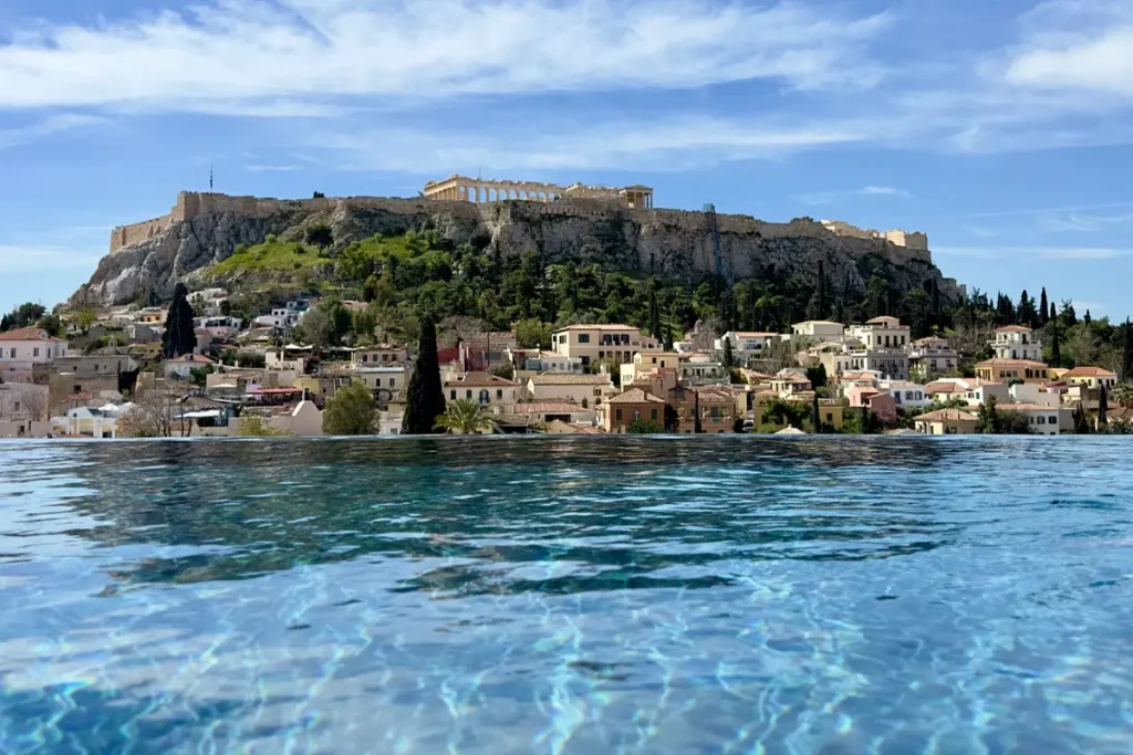 Blue water in The Dolli’s rooftop infinity pool with the Acropolis rising beyond the city.