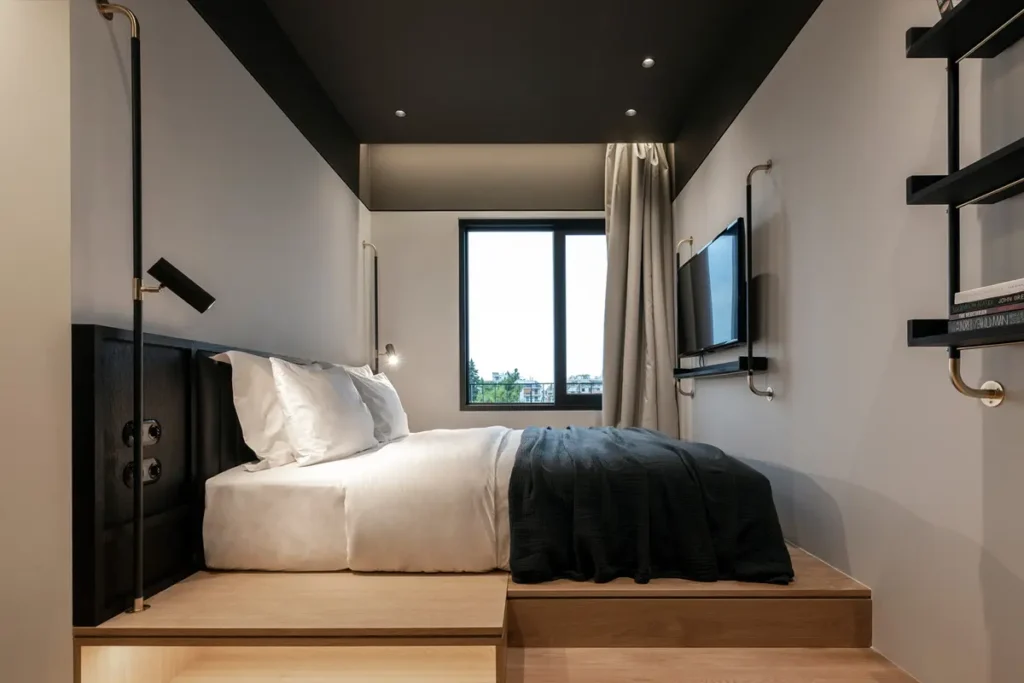 A compact bedroom with a wooden bed platform, dark ceiling and open storage at The Modernist Athens.