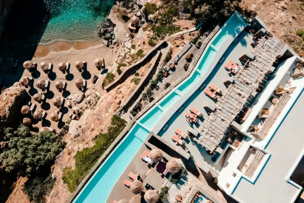 Aerial view of The Wild's long pool, cliffside terraces and sandy cove with umbrellas