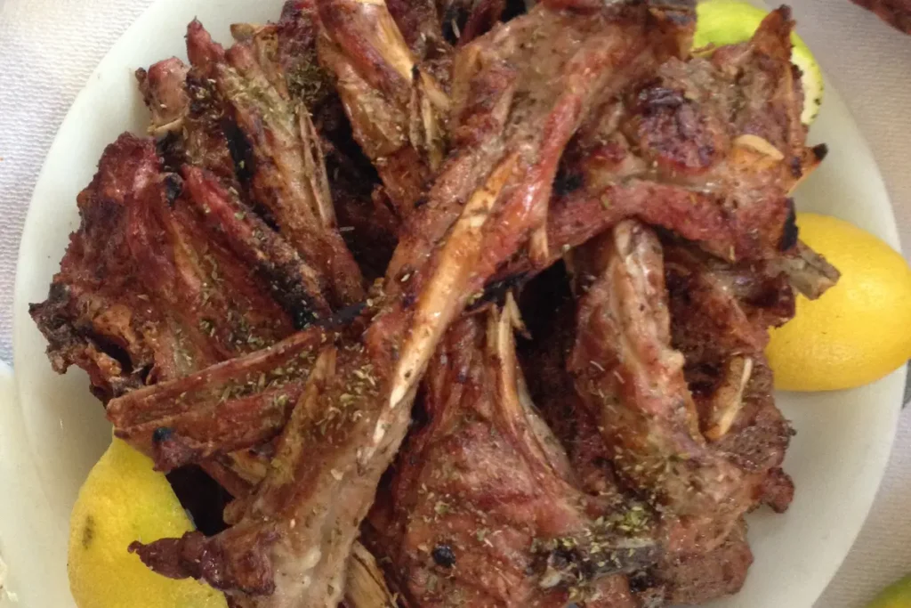 A white plate piled with grilled lamb chops and lemon at To Steki tou Elias.