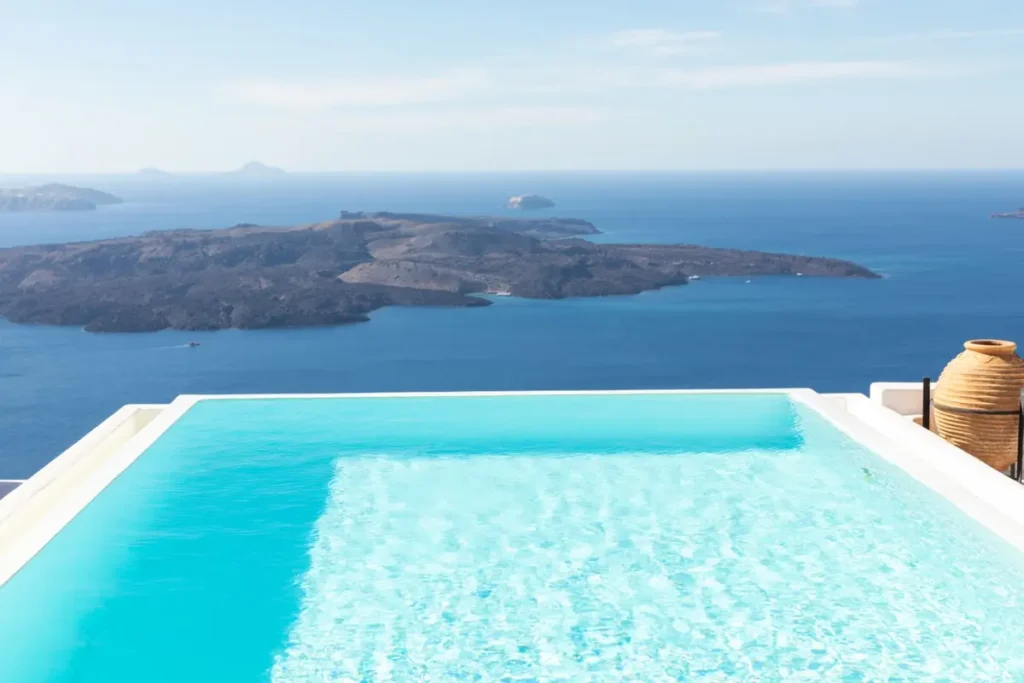 Turquoise rooftop pool with a white rim overlooking Santorini’s volcanic islands at Tsitouras Collection.