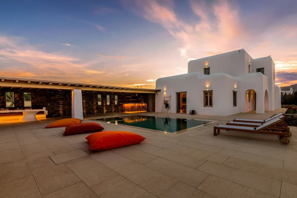 Pool, loungers and floor cushions outside Villa Aloni beneath a pink evening sky