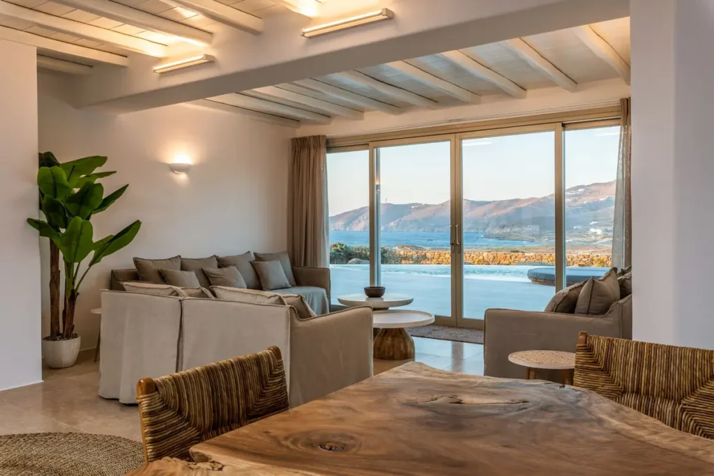 Sofas and a wooden table beneath white ceiling beams, with sea views through Villa Mati's windows