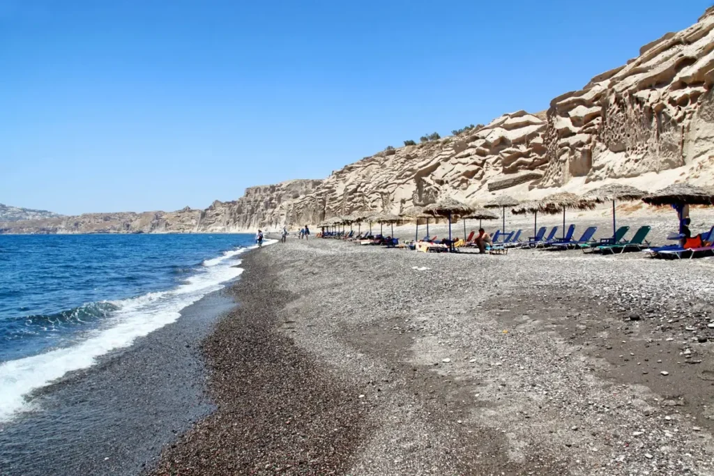 Pale wind-sculpted cliffs above the dark sand and pebbles of Vlychada Beach.