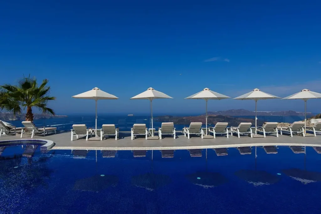 Blue swimming pool with sun loungers and white umbrellas overlooking the sea at Volcano View Hotel.