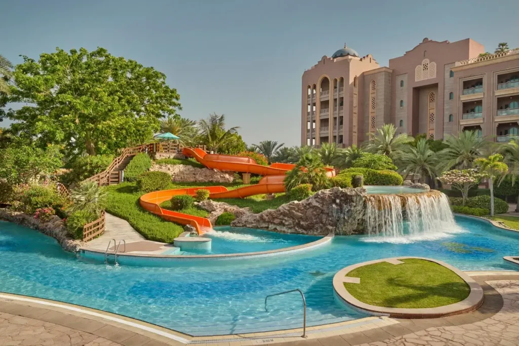 Curving pool, waterfall, waterslide, and palm trees beside the palace at Emirates Palace Mandarin Oriental, Abu Dhabi.