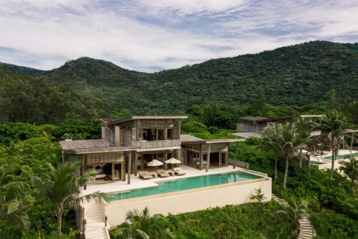 Timber villa with a long private pool and sun loungers beneath forested hills at Six Senses Con Dao