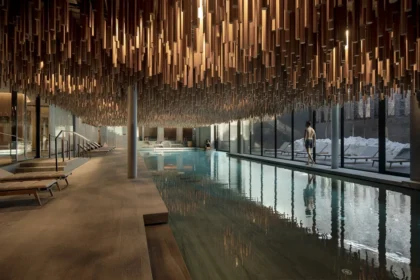 Indoor swimming pool beneath suspended wooden elements with large windows along one side at Six Senses Crans-Montana