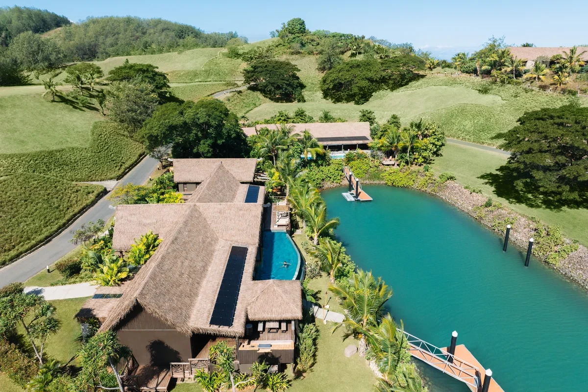 Aerial view of a thatched residence with a pool beside a turquoise marina at Six Senses Fiji