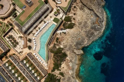Overhead view of an angular swimming pool beside a rocky coast and deep blue water at Six Senses Ibiza