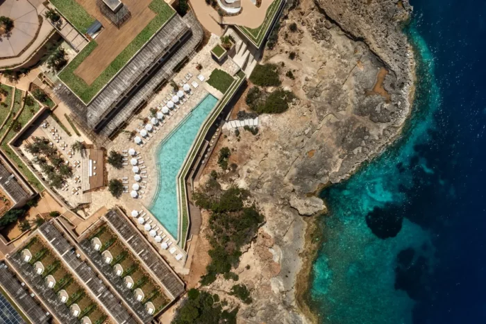 Overhead view of an angular swimming pool beside a rocky coast and deep blue water at Six Senses Ibiza