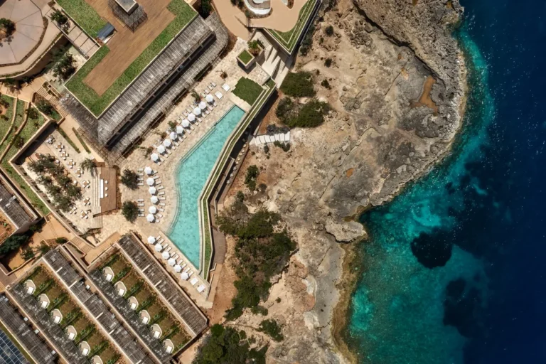 Overhead view of an angular swimming pool beside a rocky coast and deep blue water at Six Senses Ibiza
