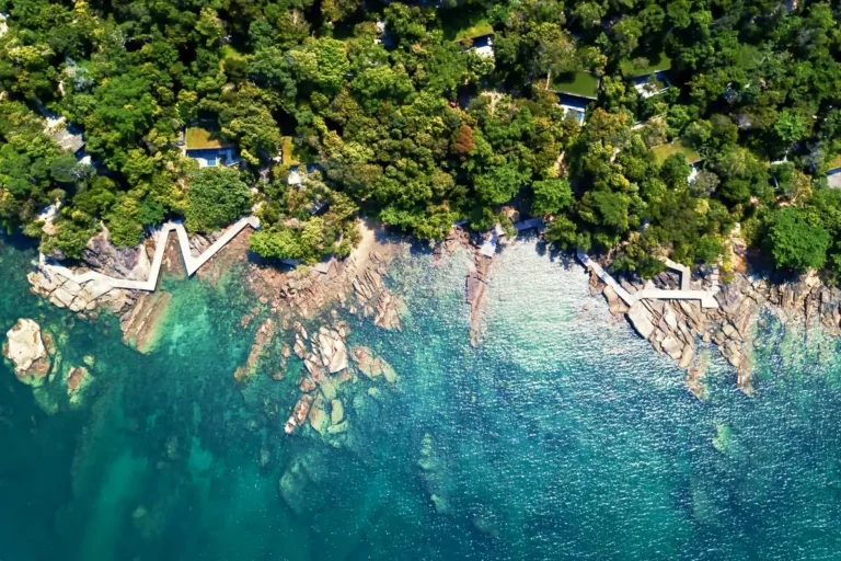 Overhead view of dense island forest, rocky shallows, and a waterfront walkway at Six Senses Krabey Island
