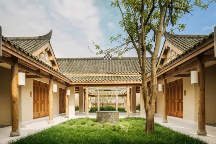 Tree in a grassy courtyard framed by timber doors and gray tiled roofs at Six Senses Qing Cheng Mountain