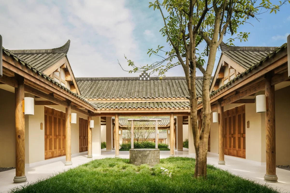 Tree in a grassy courtyard framed by timber doors and gray tiled roofs at Six Senses Qing Cheng Mountain