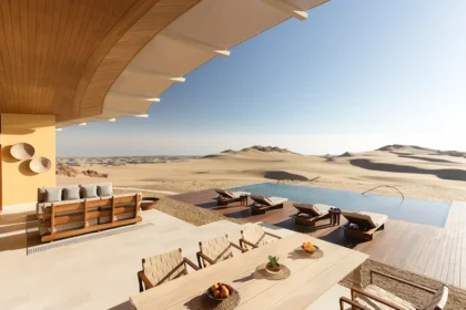 Shaded dining terrace and lounge seating facing an infinity pool and sand dunes at Six Senses Southern Dunes, The Red Sea