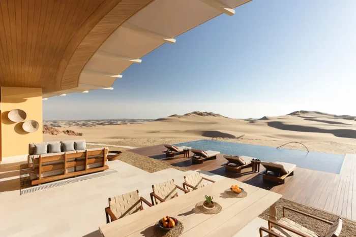 Shaded dining terrace and lounge seating facing an infinity pool and sand dunes at Six Senses Southern Dunes, The Red Sea