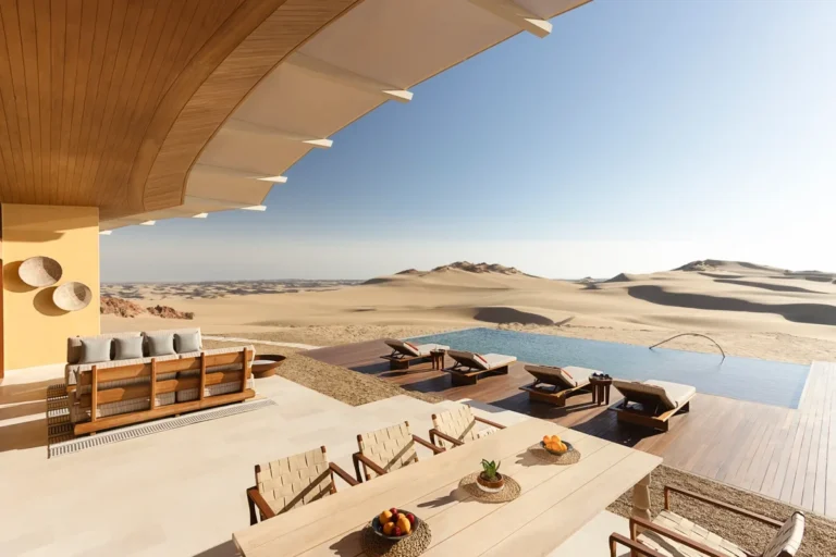 Shaded dining terrace and lounge seating facing an infinity pool and sand dunes at Six Senses Southern Dunes, The Red Sea