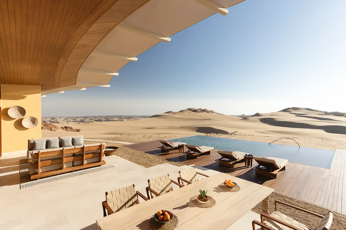 Shaded dining terrace and lounge seating facing an infinity pool and sand dunes at Six Senses Southern Dunes, The Red Sea
