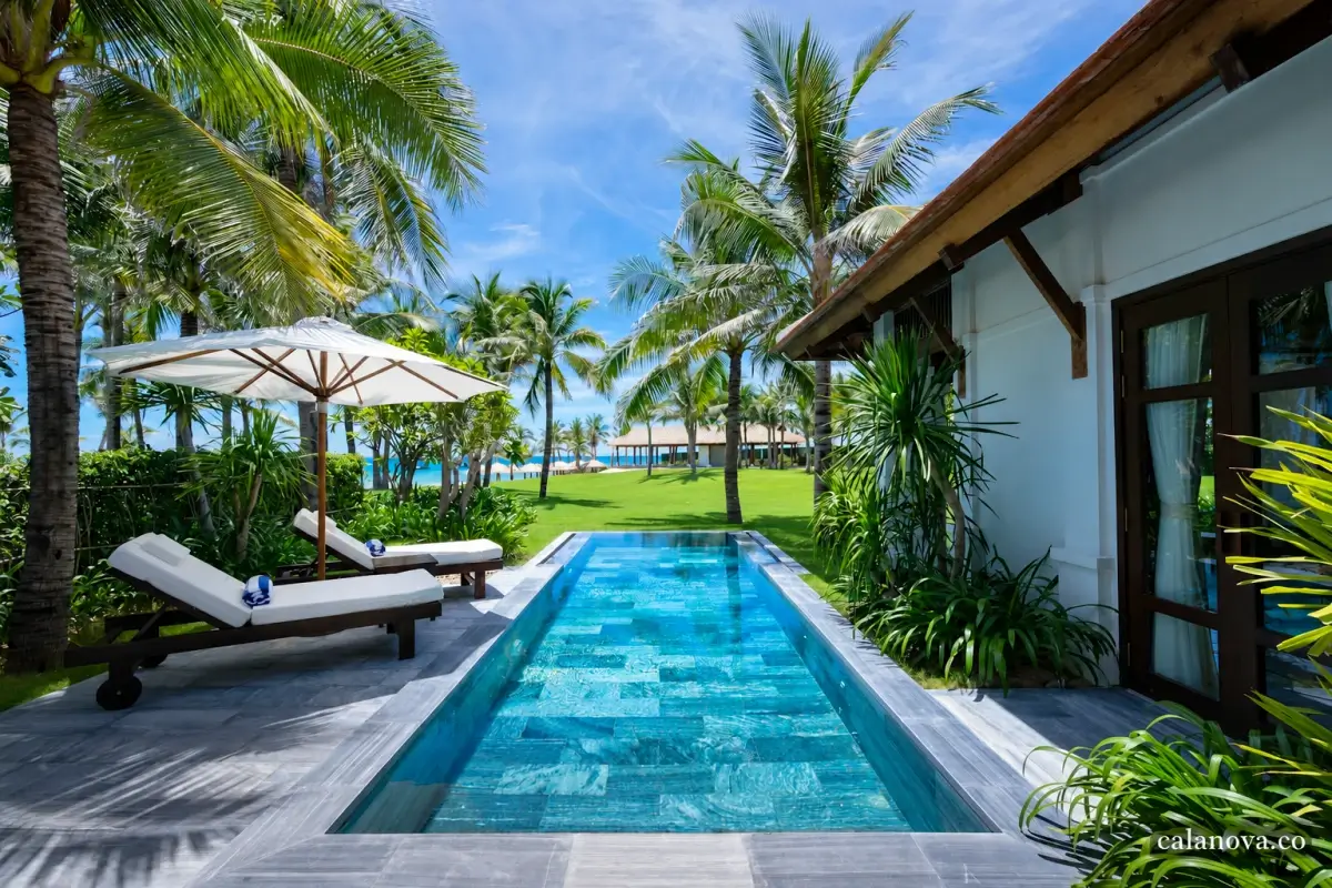 A private pool beside a villa, with two shaded loungers, palm trees and a view towards the sea.