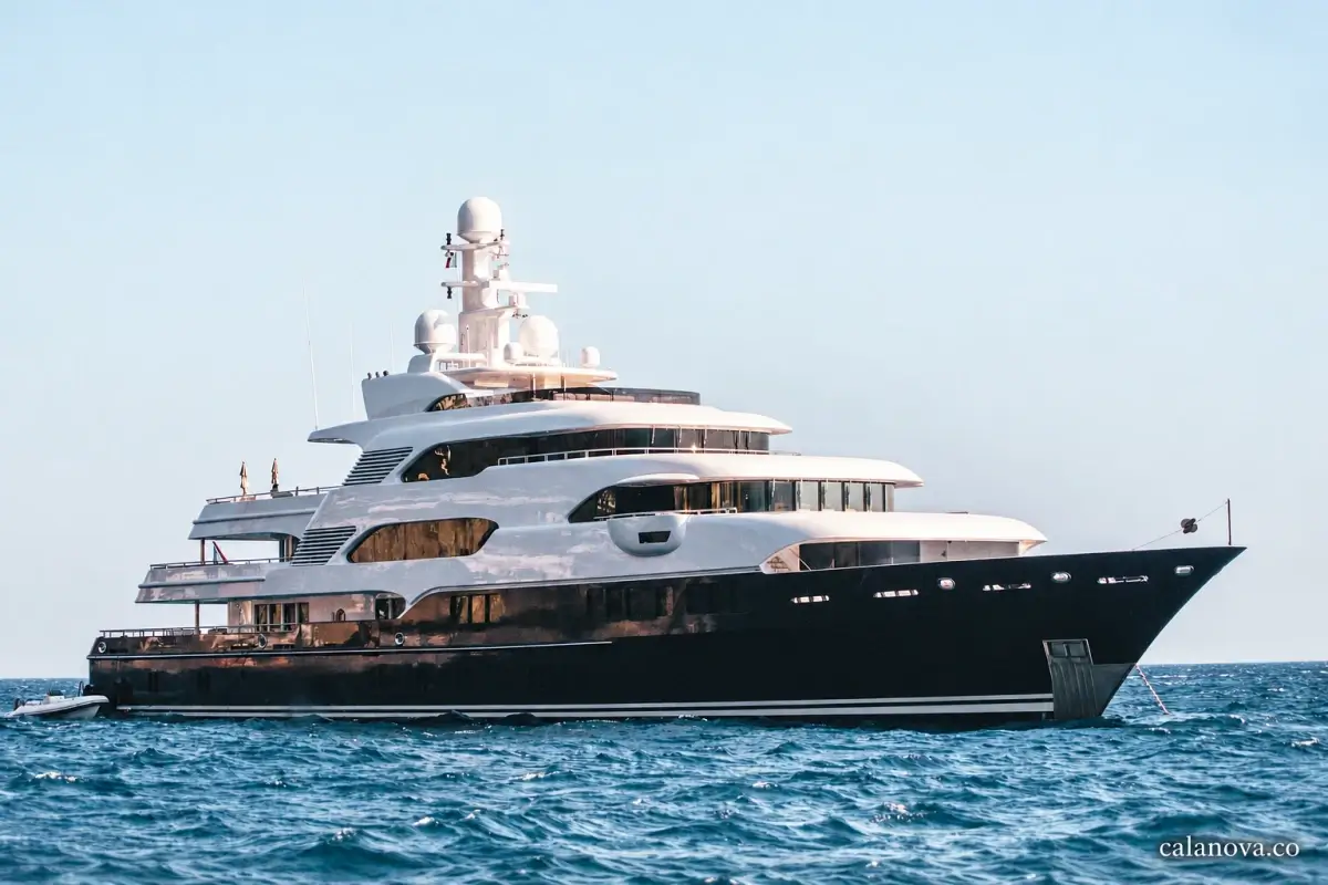 A large motor yacht with a dark hull and white upper decks anchored on blue water.