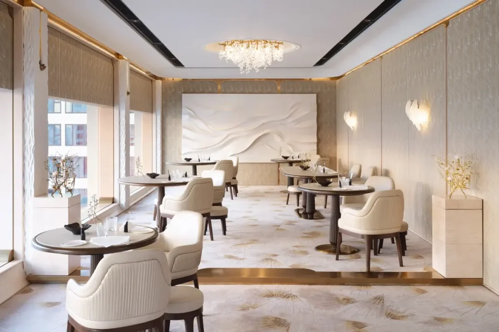 Round dining tables, pale upholstered chairs, and a sculptural wall feature at Anne-Sophie Pic at Le Normandie, Mandarin Oriental, Bangkok.