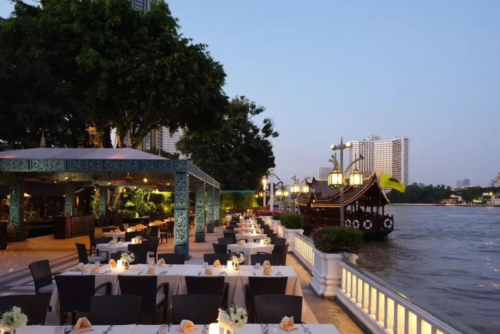 Tables set beside the Chao Phraya River and a moored hotel boat at Terrace Rim Naam, Mandarin Oriental, Bangkok.