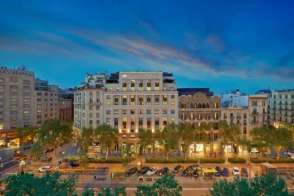 Illuminated facade of Mandarin Oriental, Barcelona facing Passeig de Gràcia, with traffic, trees, and neighboring buildings at dusk.