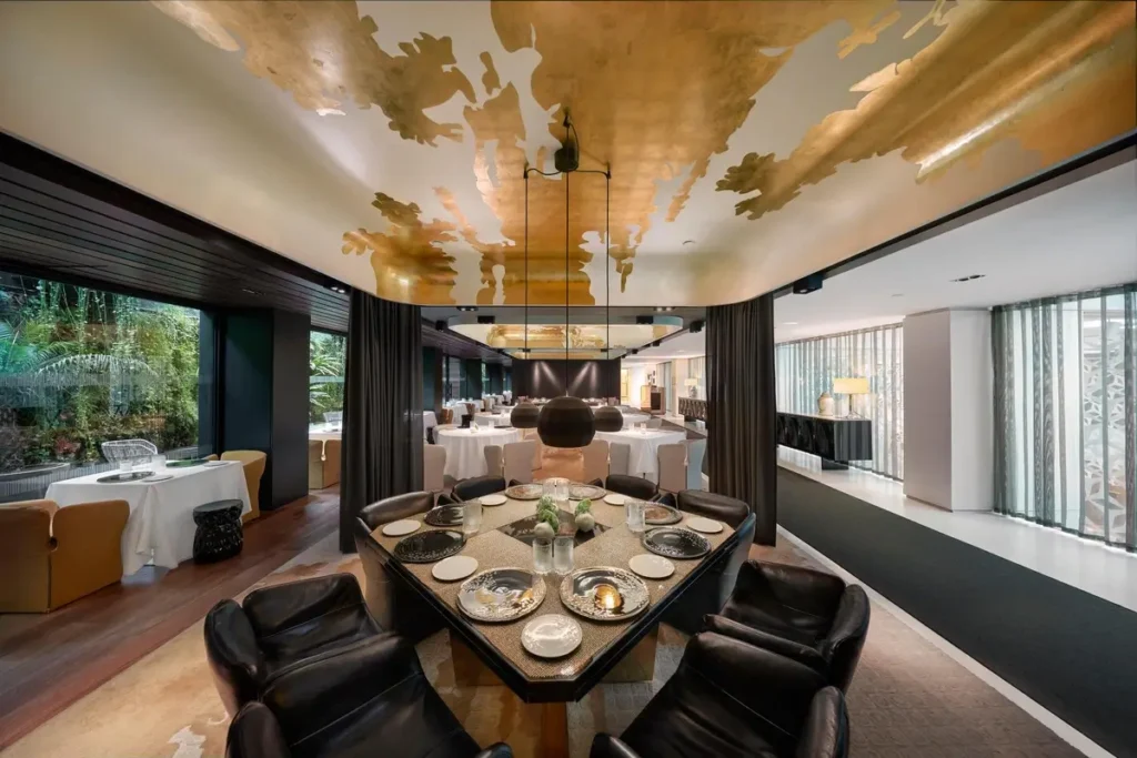 Set dining tables, dark upholstered chairs, and a gold-toned ceiling inside Moments at Mandarin Oriental, Barcelona.