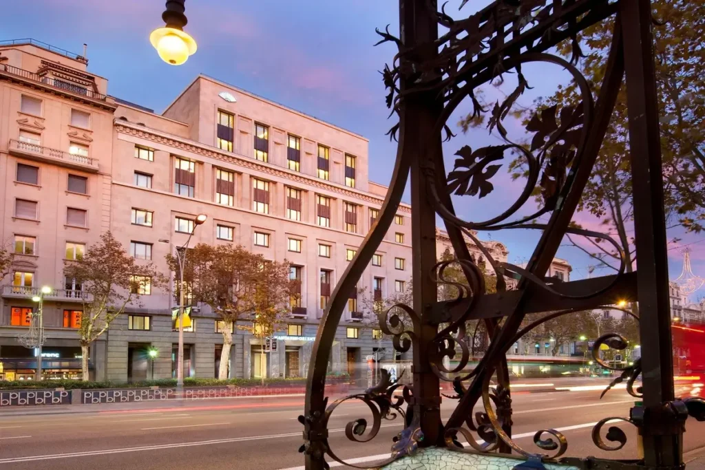 Mandarin Oriental, Barcelona across Passeig de Gràcia, framed by decorative ironwork with traffic light trails along the avenue.