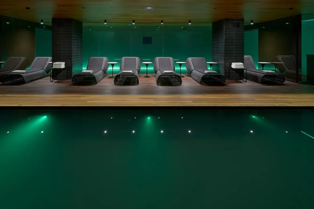 Dark indoor swimming pool with underwater lights and loungers along the far side at Mandarin Oriental, Barcelona.