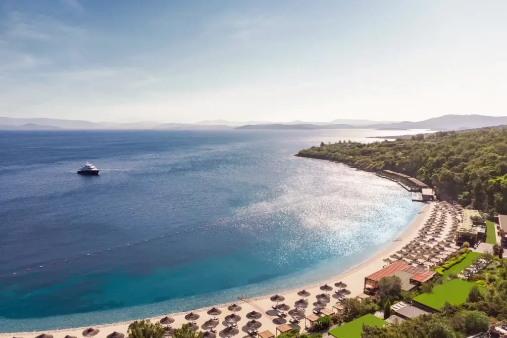 Curved sandy beach lined with loungers and umbrellas beside blue Aegean water at Mandarin Oriental, Bodrum.