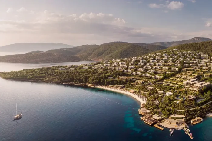 Aerial view of Mandarin Oriental, Bodrum spreading across a wooded hillside above a curved Aegean bay.