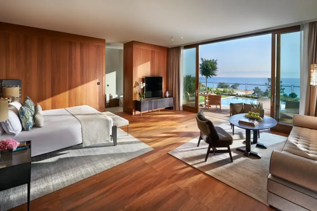 Open-plan Mandarin Junior Suite with a bed, seating area, wood floors, and broad windows toward the sea.