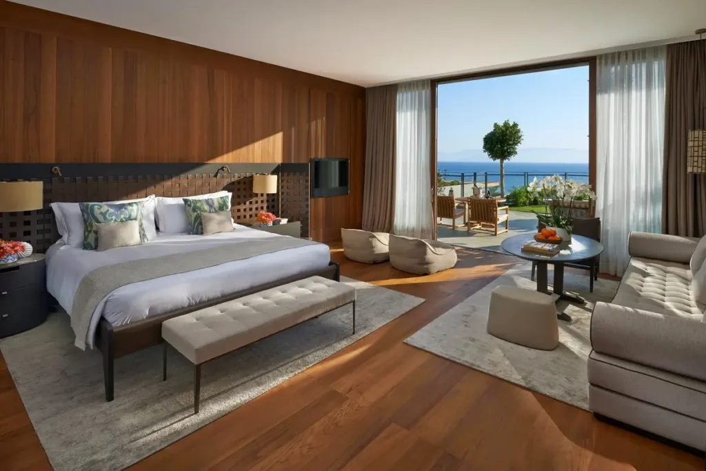 Bed, upholstered seating, wood paneling, and glass doors facing a sea-view terrace in a Sea View Room.