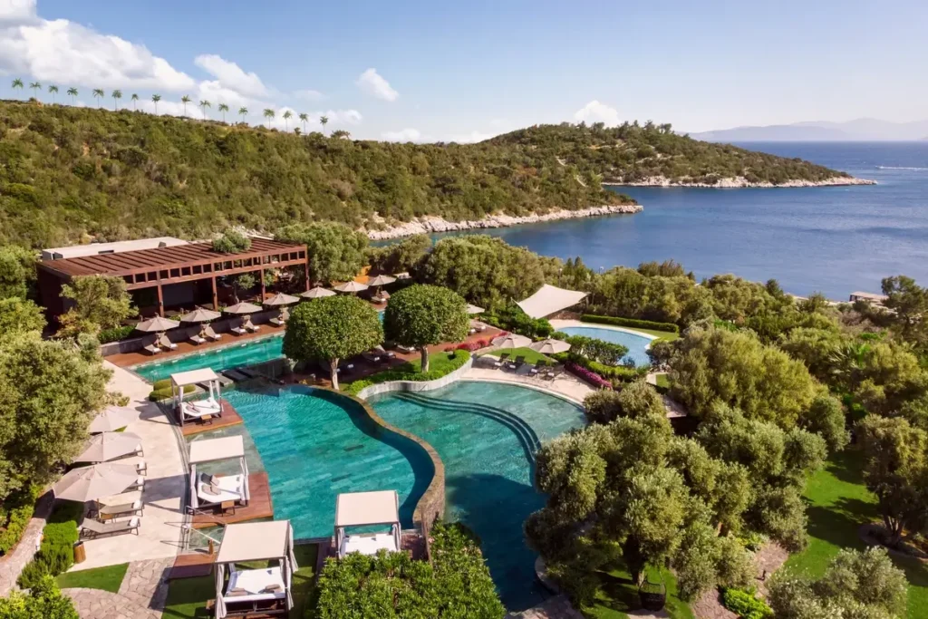 Outdoor pools, loungers, landscaped terraces, and low-rise resort buildings overlooking the sea.
