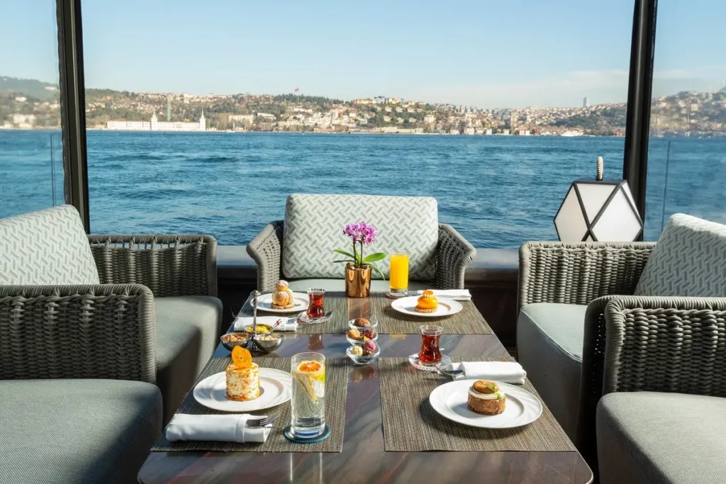 Wicker armchairs and a table set with drinks and pastries facing the strait in a Bosphorus Lounge cabana at Mandarin Oriental Bosphorus, Istanbul.