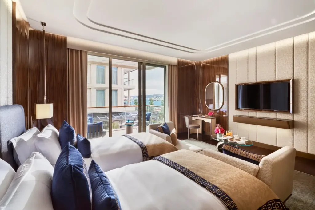 Twin beds, wood-paneled walls, and balcony doors looking toward the water in a Deluxe Bosphorus Room at Mandarin Oriental Bosphorus, Istanbul.