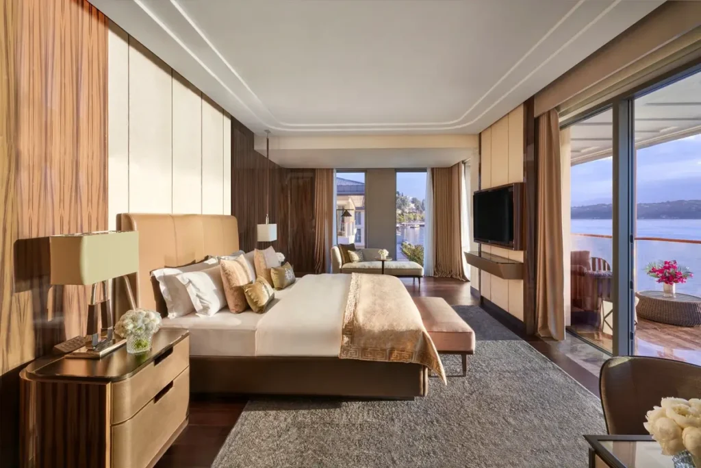 Bed, chaise longue, and glass doors opening to a water-facing balcony in a One Bedroom Bosphorus Suite at Mandarin Oriental Bosphorus, Istanbul.