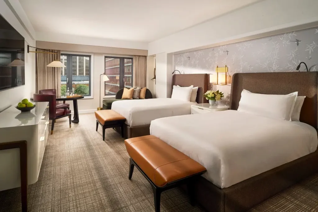 Two beds, a desk, and seating beside the window in a Premier Deluxe Double Room at Mandarin Oriental, Boston.