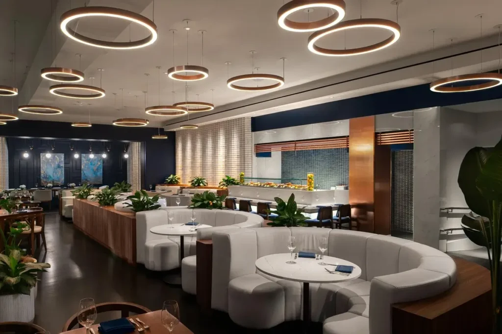 Curved upholstered booths, set tables, and circular ceiling lights inside Ramsay’s Kitchen at Mandarin Oriental, Boston.