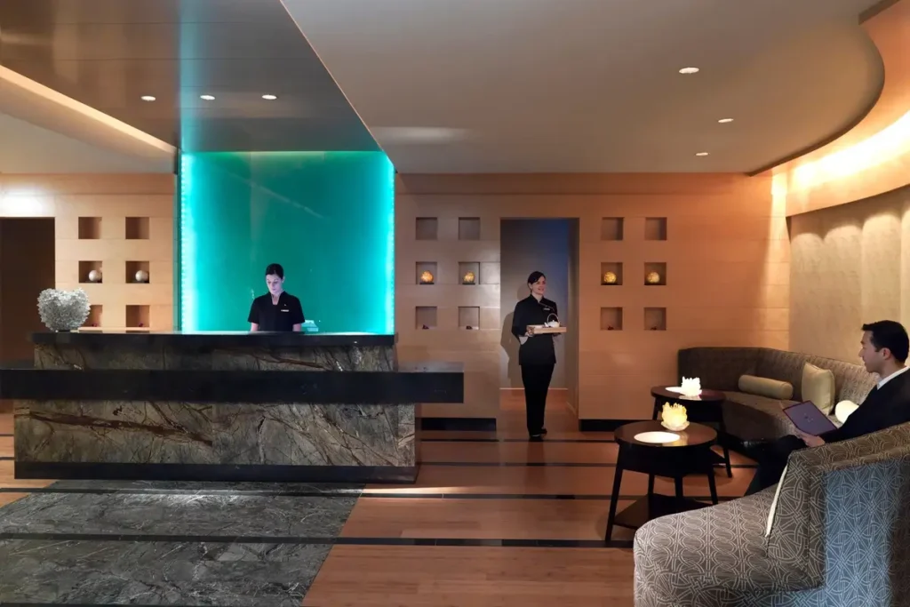 Curved reception desk, turquoise-lit feature, and seating in the spa lobby at Mandarin Oriental, Boston.
