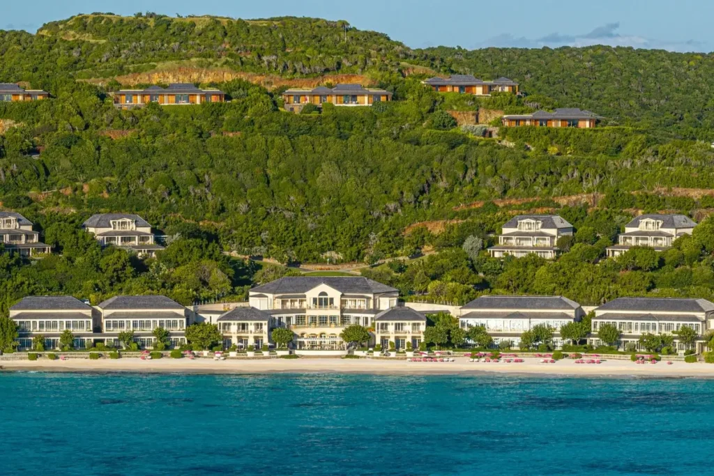Mandarin Oriental, Canouan’s beachfront buildings and landscaped hillside viewed from over the water.