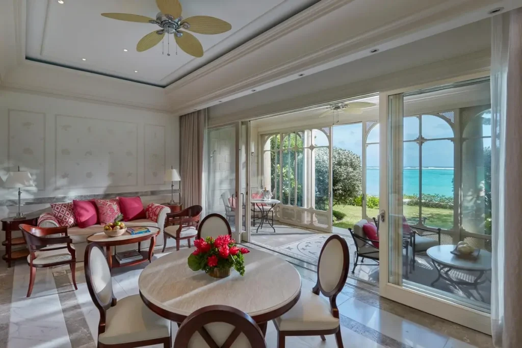Dining table, pink-cushioned seating, and glass doors facing the coast in a Beachfront Suite at Mandarin Oriental, Canouan.