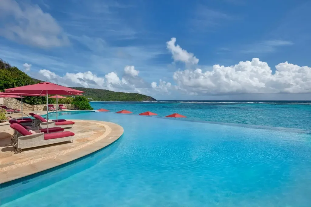 Blue infinity pool, pink loungers, and umbrellas beside the sea at Mandarin Oriental, Canouan.