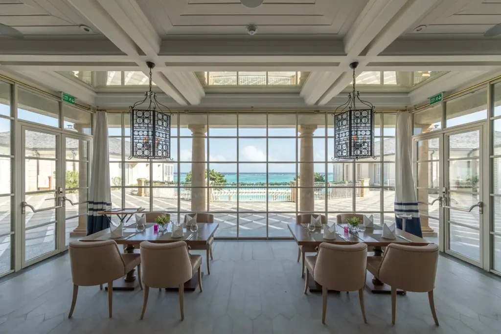 Dining tables, upholstered chairs, and broad windows overlooking the ocean at TIDES, Mandarin Oriental, Canouan.