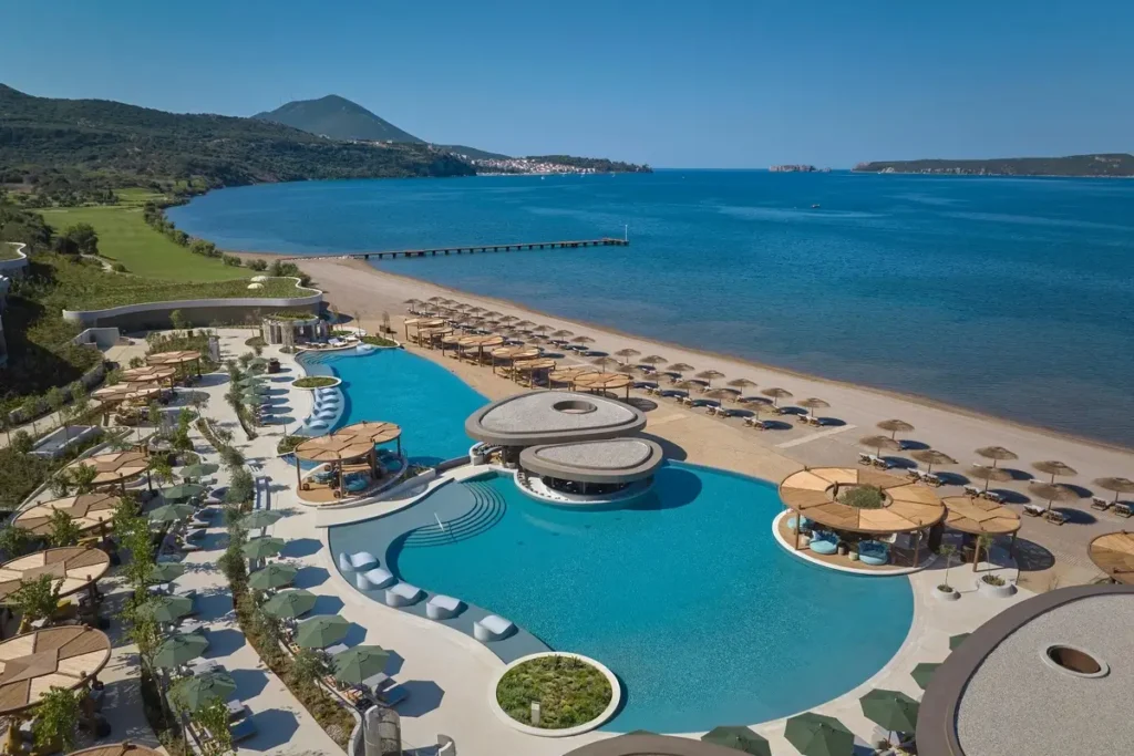 Curved swimming pool, loungers, sandy beach, and Navarino Bay at Ormos Beach Club.