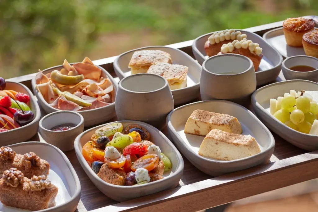 Small bowls and plates of fruit, bread, pastries, and other breakfast dishes arranged on a serving tray.